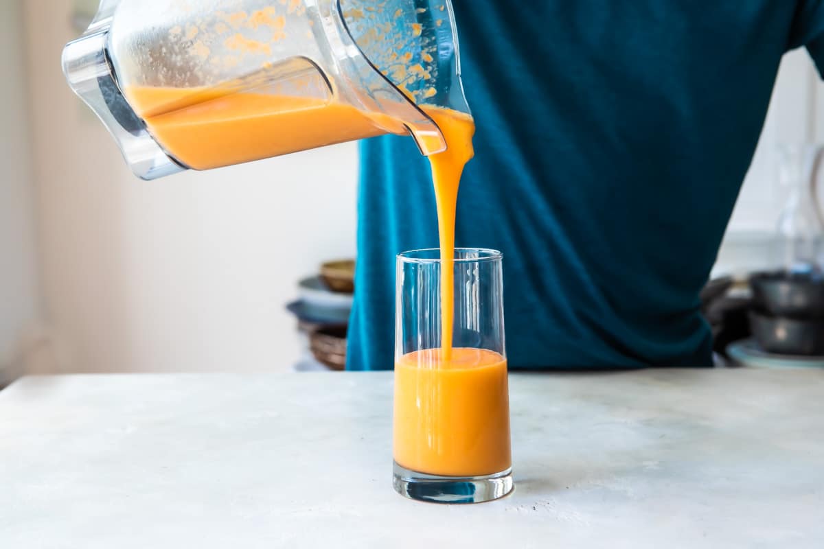 A mango carrot smoothie being poured out of a blender into a glass.