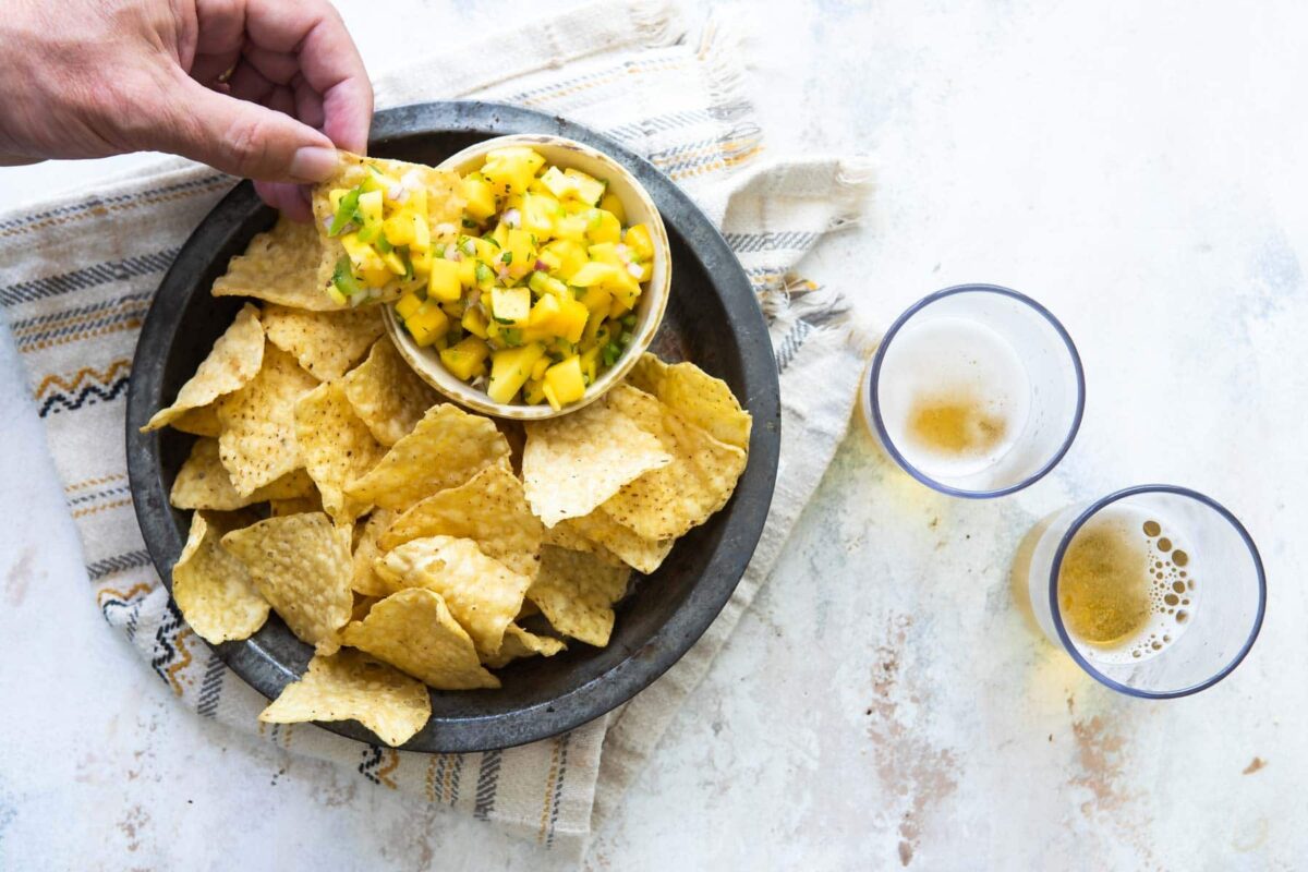 Someone scooping mango salsa out of a bowl with a tortilla chip.