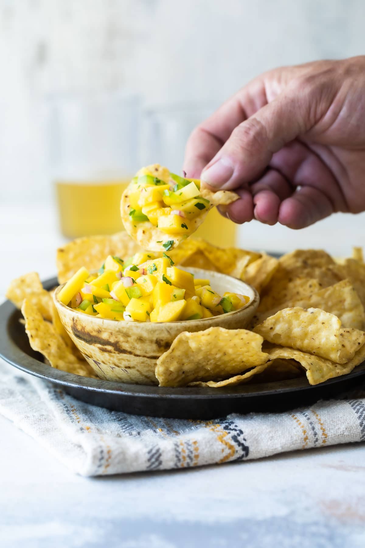 Someone scooping mango salsa out of a bowl with a tortilla chip.