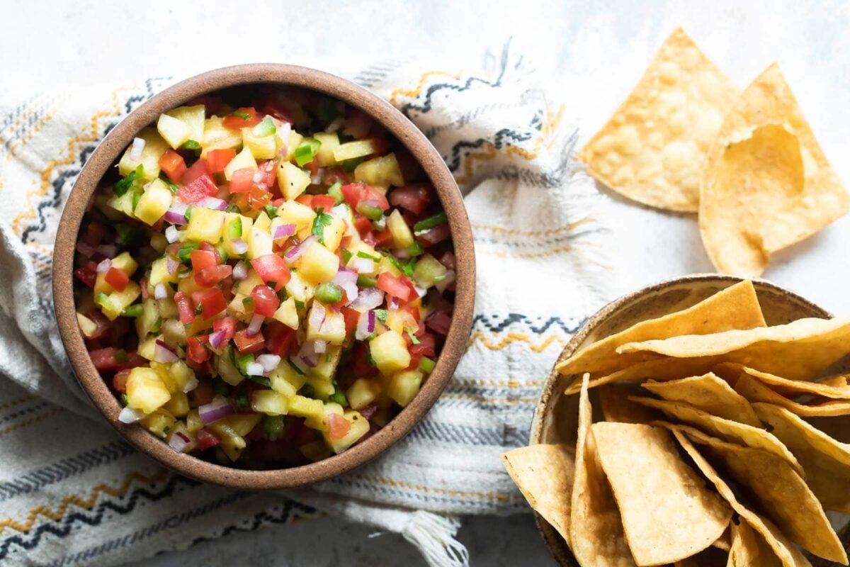 Pineapple salsa in a brown bowl next to tortilla chips.