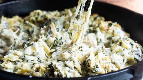 Spinach artichoke dip being scooped out of a cast iron pan.