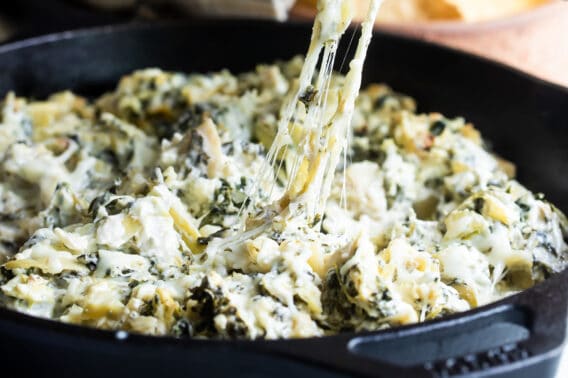 Spinach artichoke dip being scooped out of a cast iron pan.