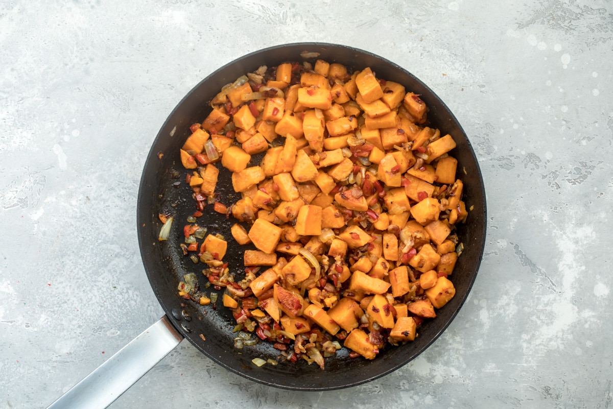 Sweet potato hash cooking in a black skillet.