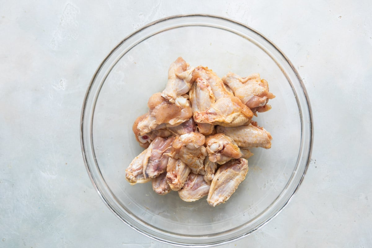 Raw chicken wings in a clear bowl.