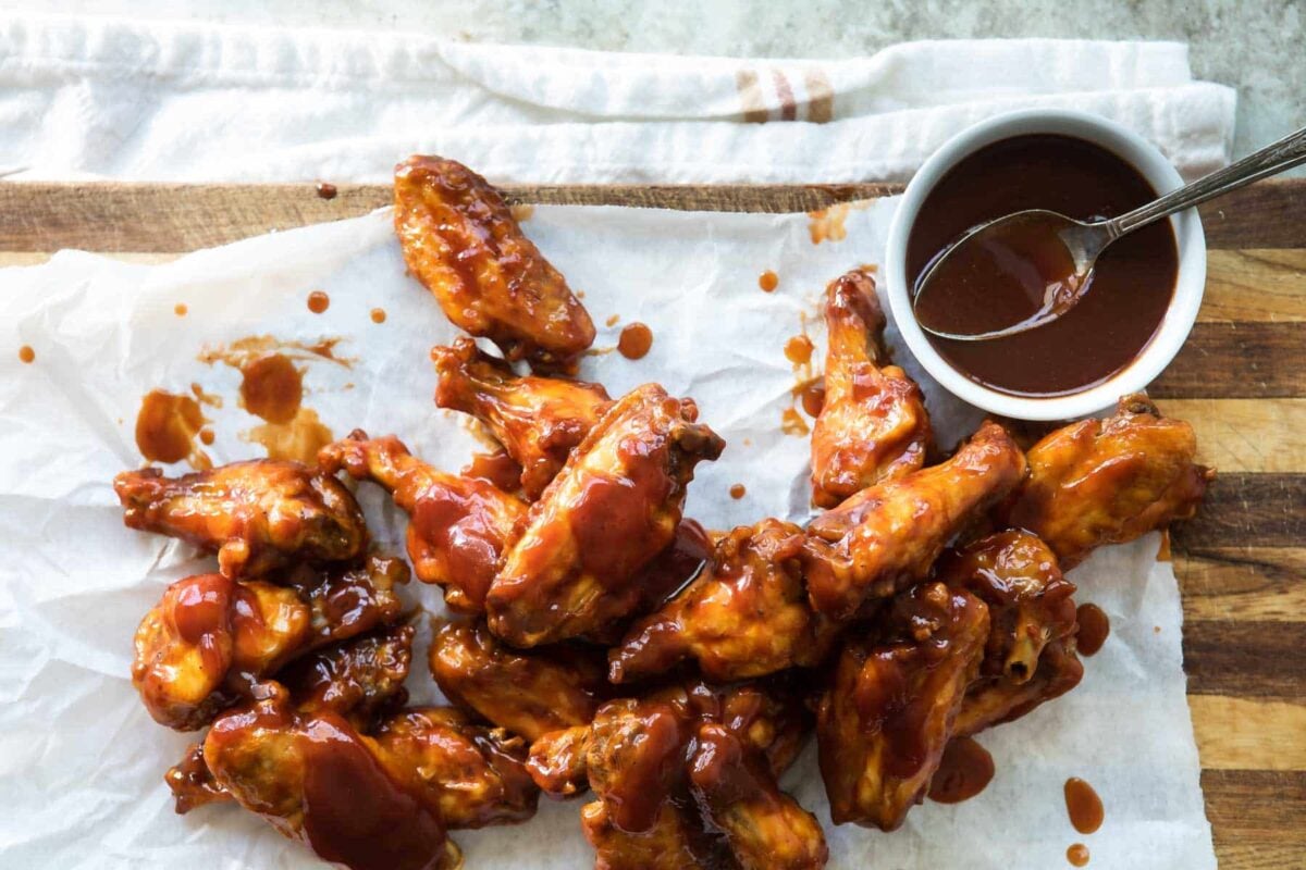 Air fryer chicken wings covered in sauce resting on parchment paper.