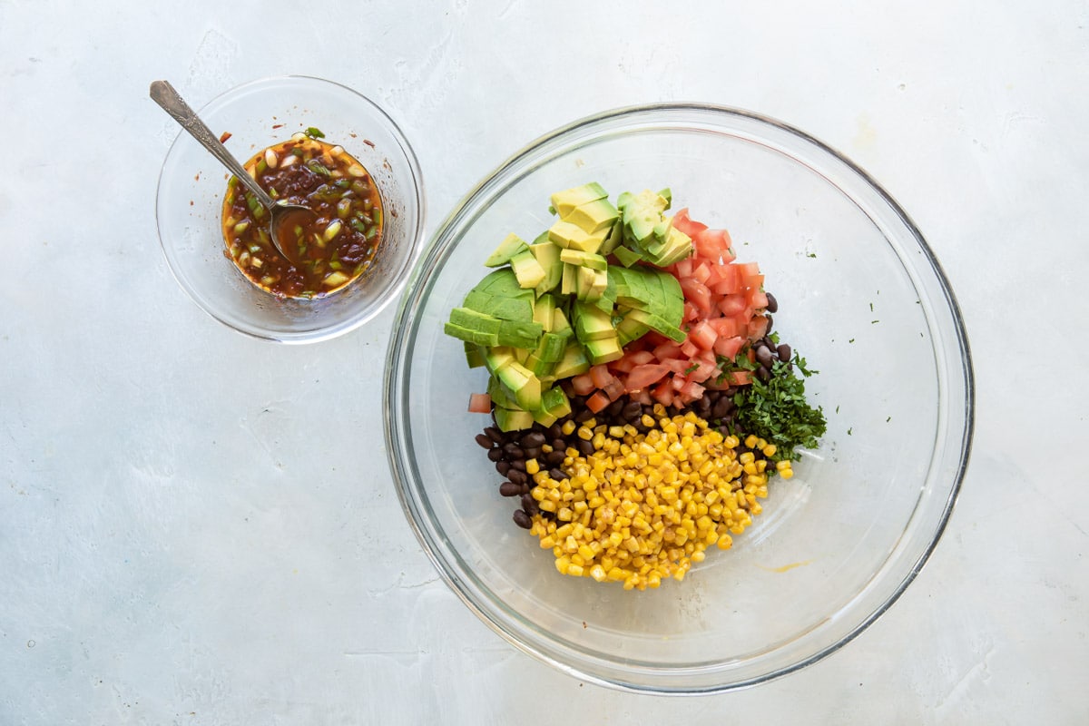 Ingredients for black bean salad in a clear bowl before being mixed.