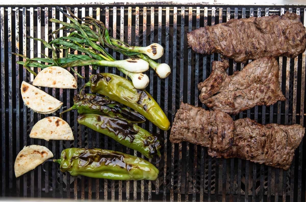 Carne Asada and vegetables roasting on a grill.