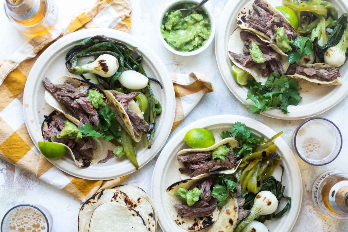 Carne Asada on a paper plates with grilled vegetables.