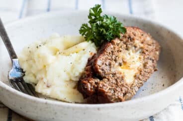 A slice of cheesy meatloaf with mashed potatoes in a low gray bowl.