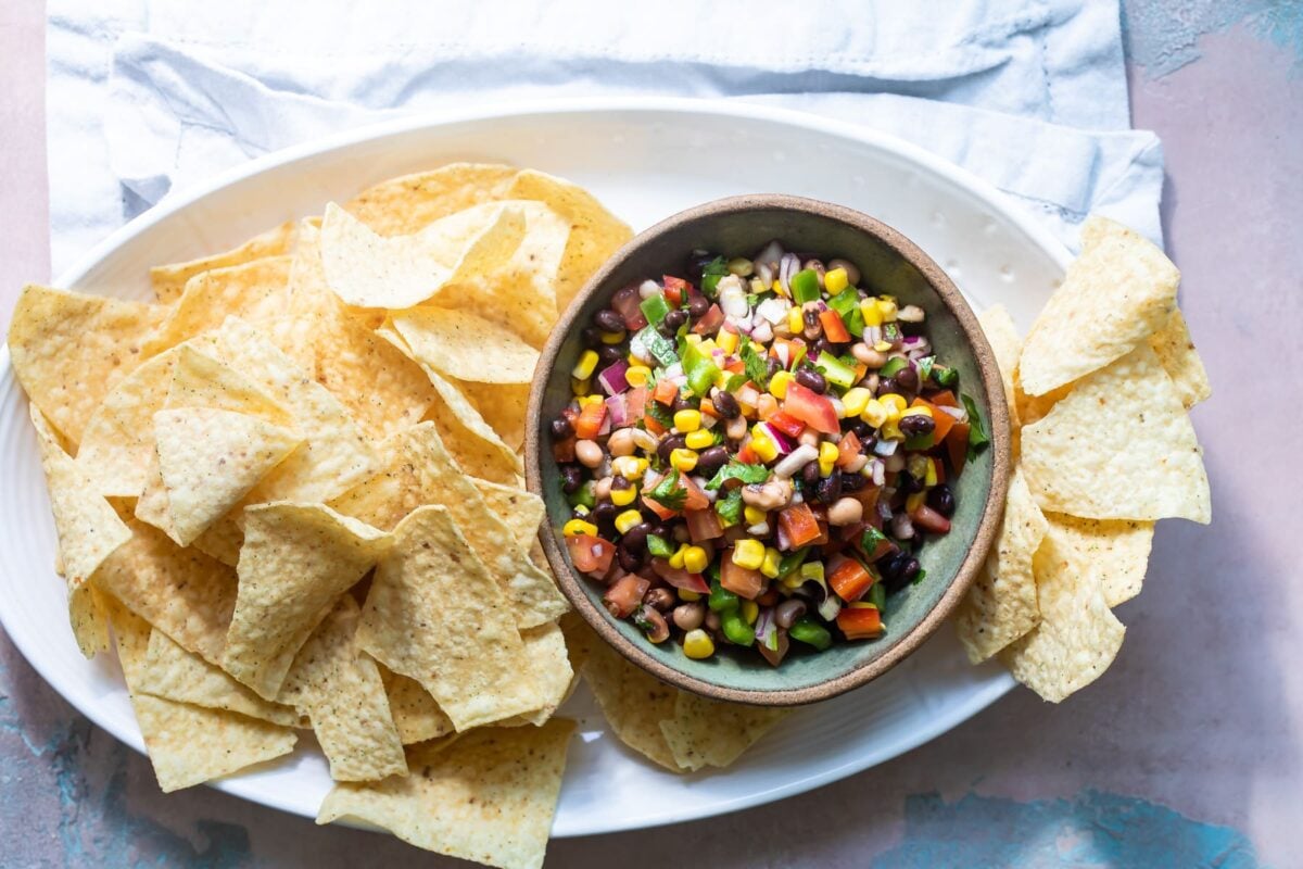 Cowboy caviar in a bowl on a white plate with tortilla chips.