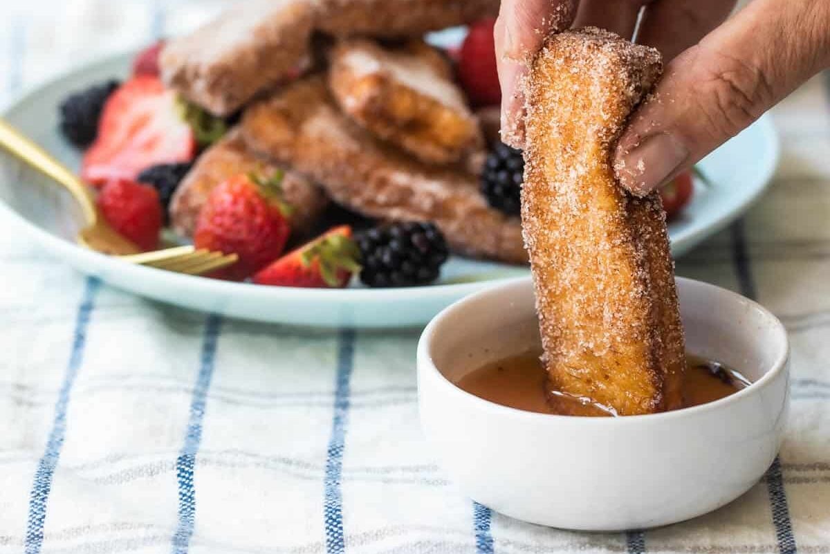 Someone dipping French toast sticks in syrup.