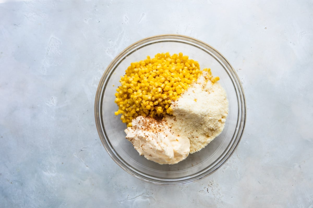 A bowl of corn, mayonnaise, Parmesan cheese, and tajin.