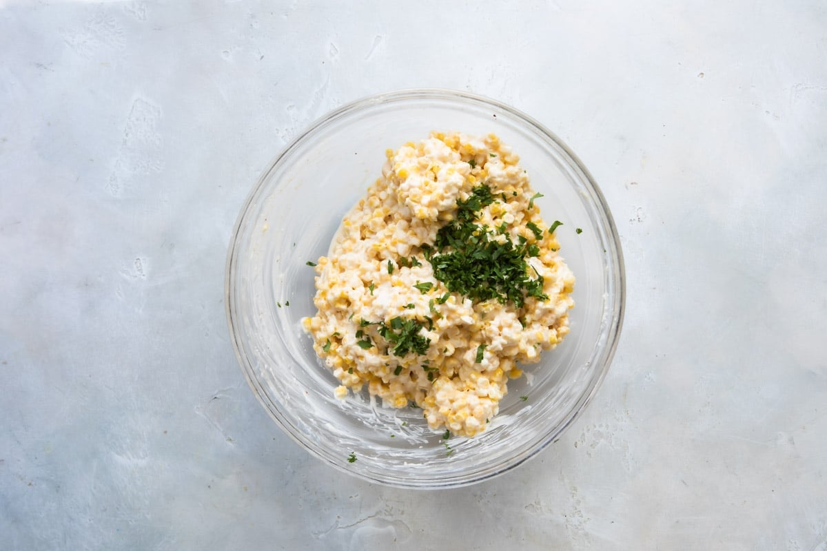 A bowl of corn, mayonnaise, Parmesan cheese, and tajin.