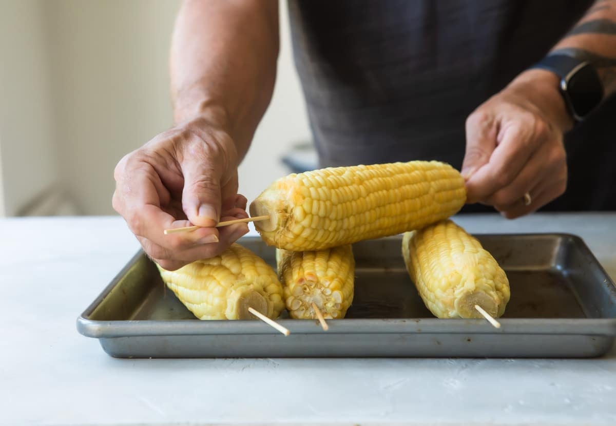 Corn on the cob on skewers, set on a baking sheet.