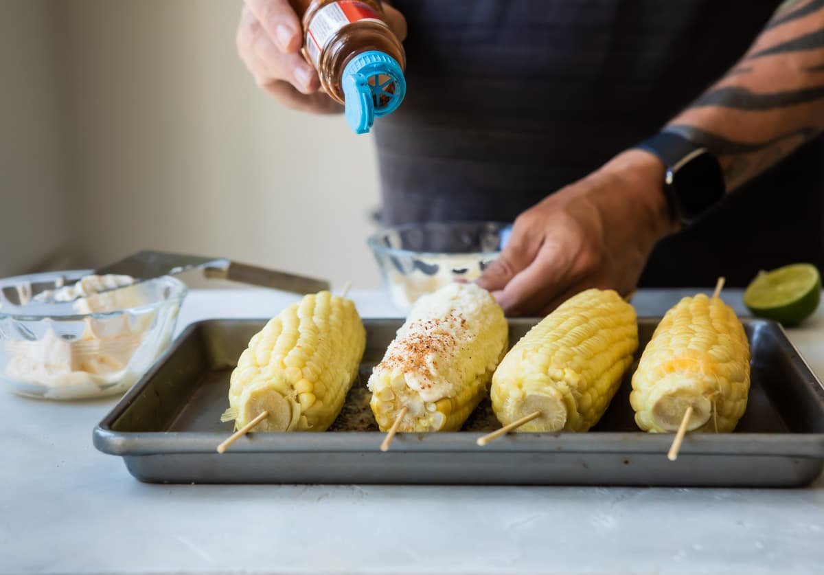 Corn on the cob on skewers, set on a baking sheet.