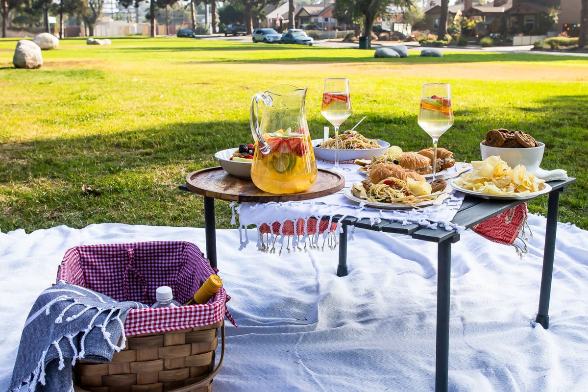 A setup for a picnic in a park with sangria and fruit salad.