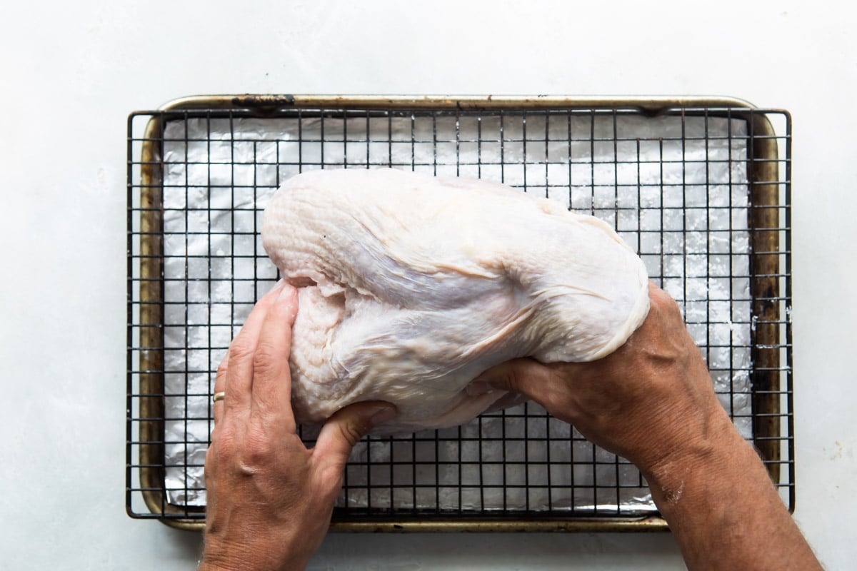 Rubbing butter and sage under the skin of a turkey breast.