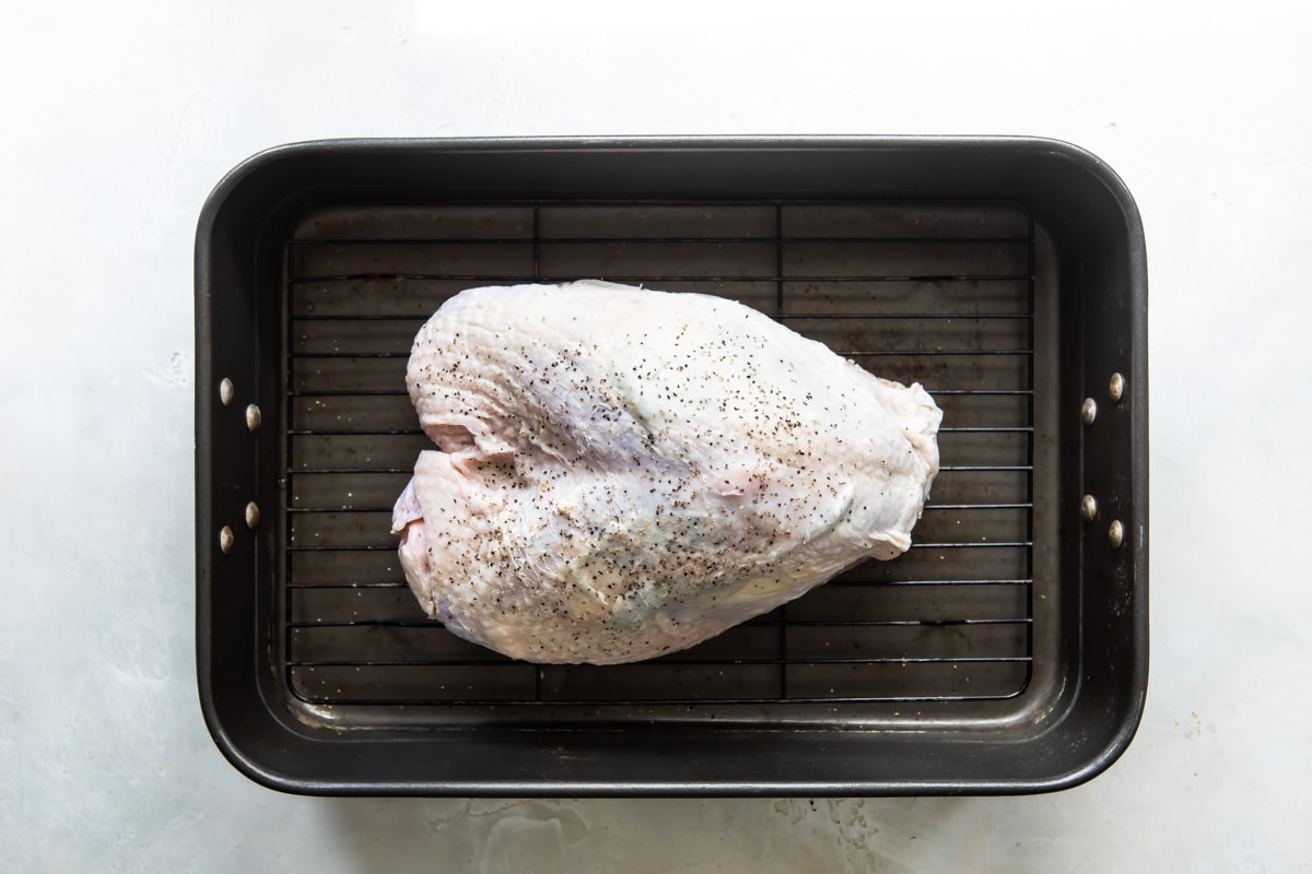 A raw turkey breast on a roasting pan.