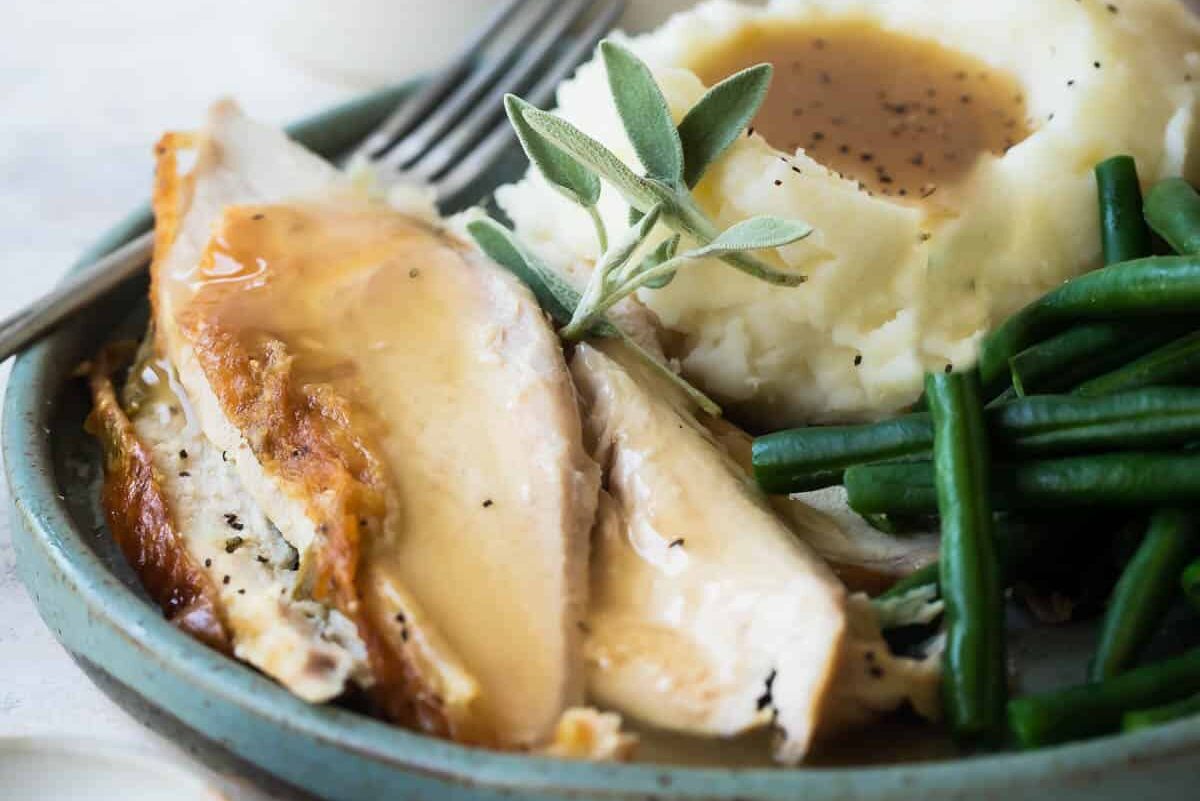 A plate of turkey breast with gravy, mashed potatoes, and green beans.