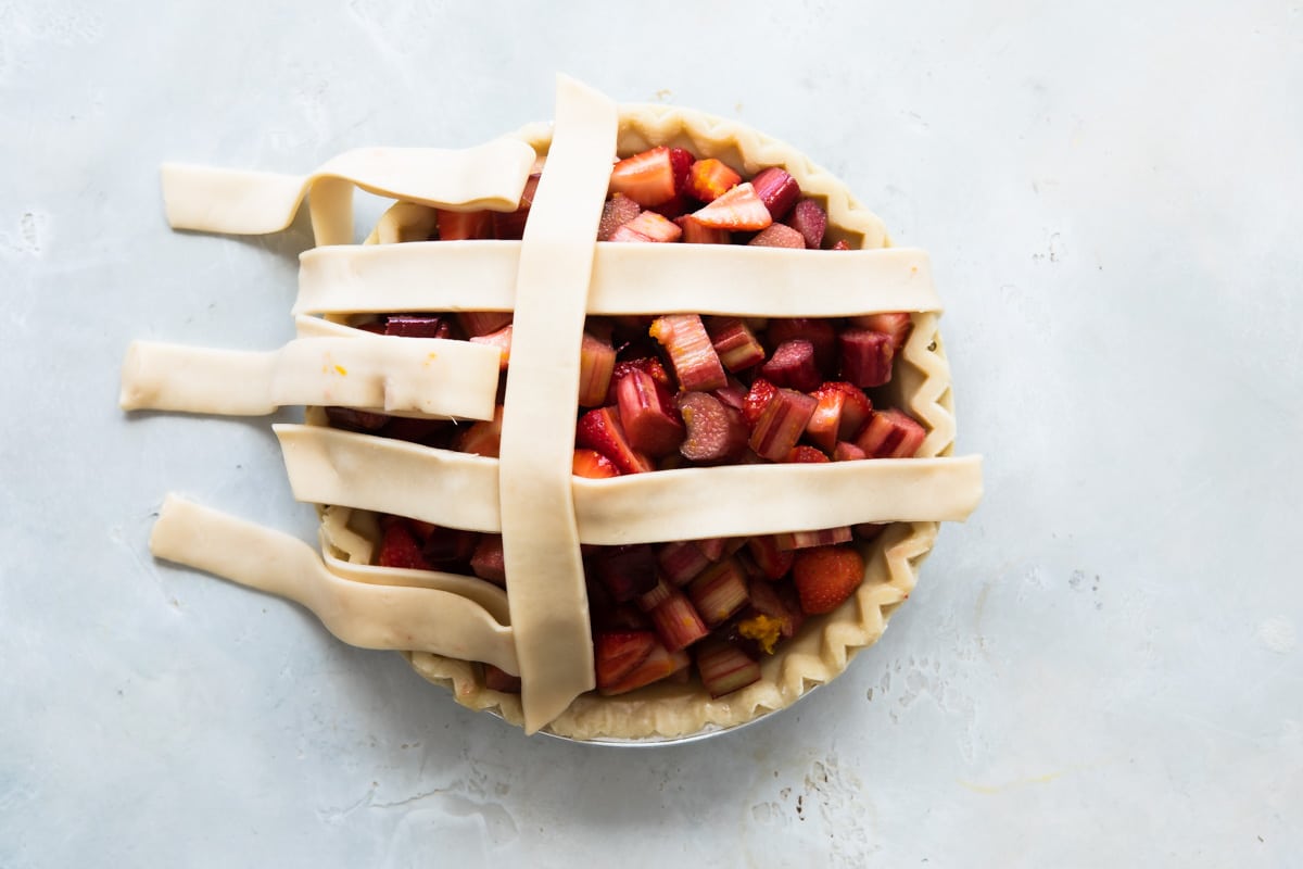 A strawberry rhubarb pie before being baked with lattice incomplete.