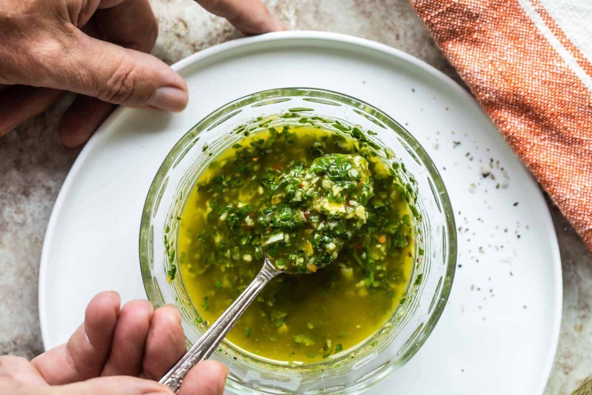 Chimichurri sauce being spooned out of a clear bowl.