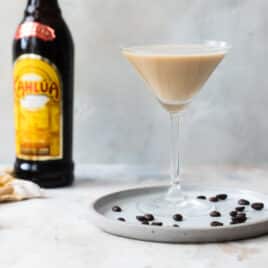 An espresso martini on a plate surrounded by espresso beans.