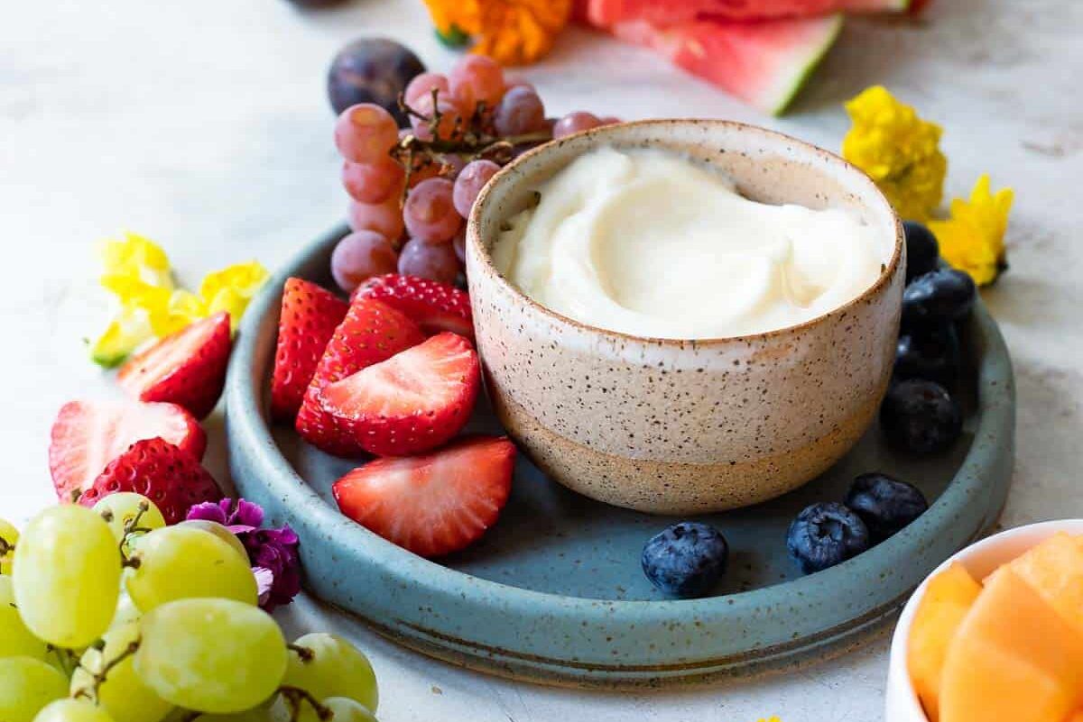 A bowl of fruit dip surrounded by fresh fruit.