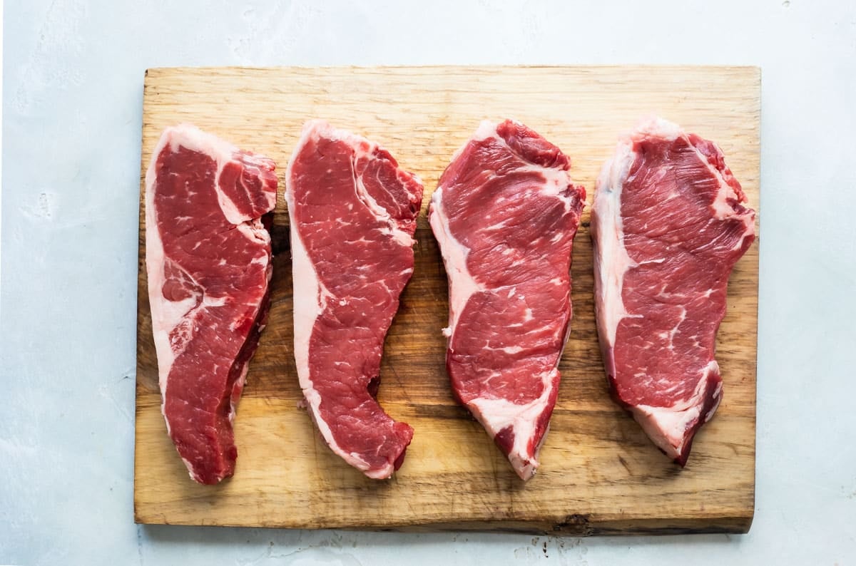 Raw New York strip steaks on a cutting board.