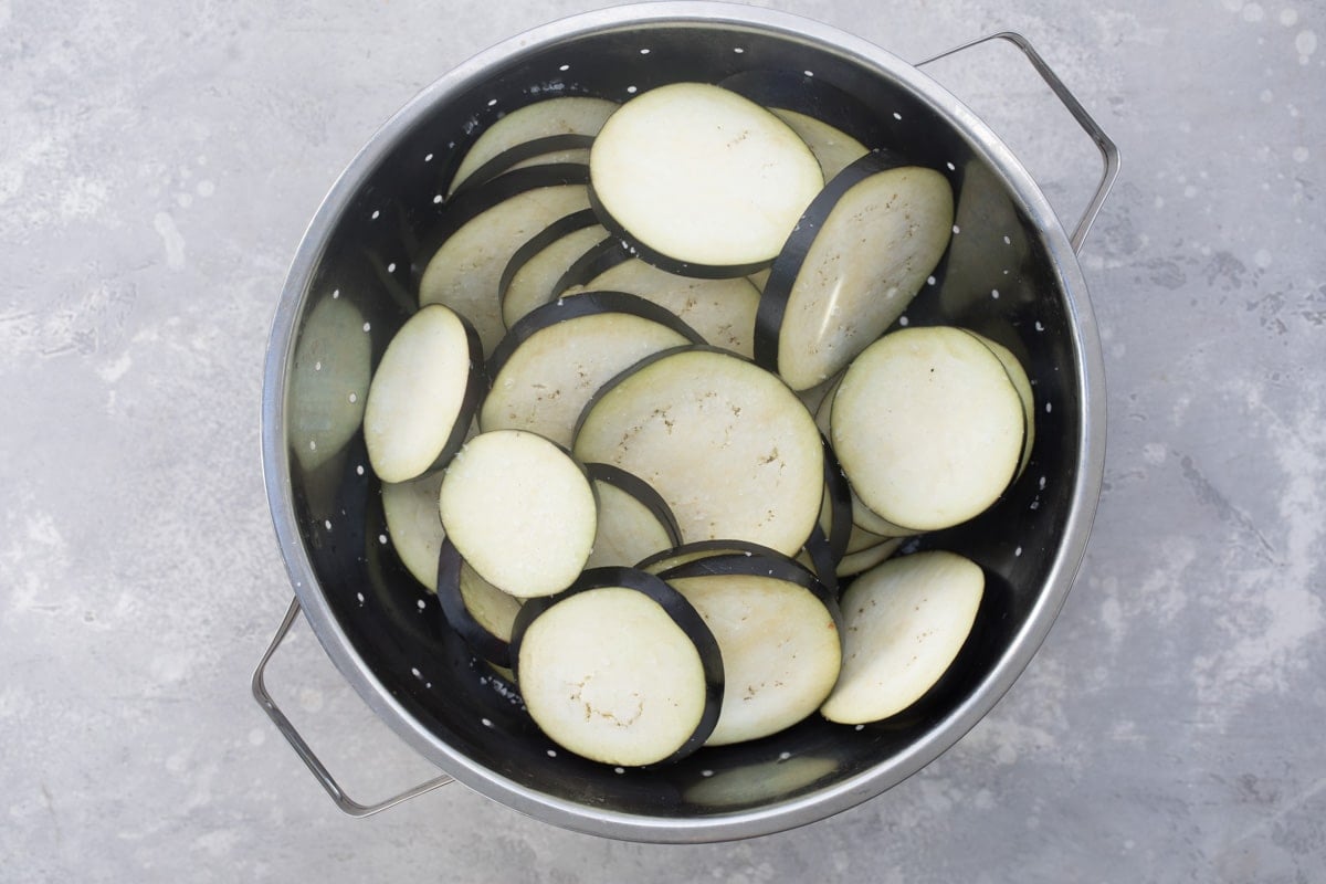 Sliced eggplant draining in a colander.