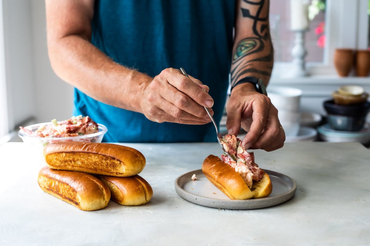 Someone filling a toasted brioche bun with lobster meat.