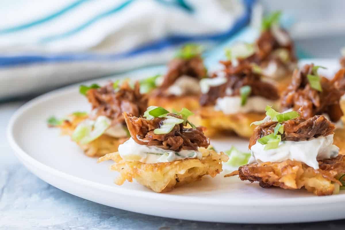 A platter of potato pancakes with bbq pulled pork and sour cream on top.