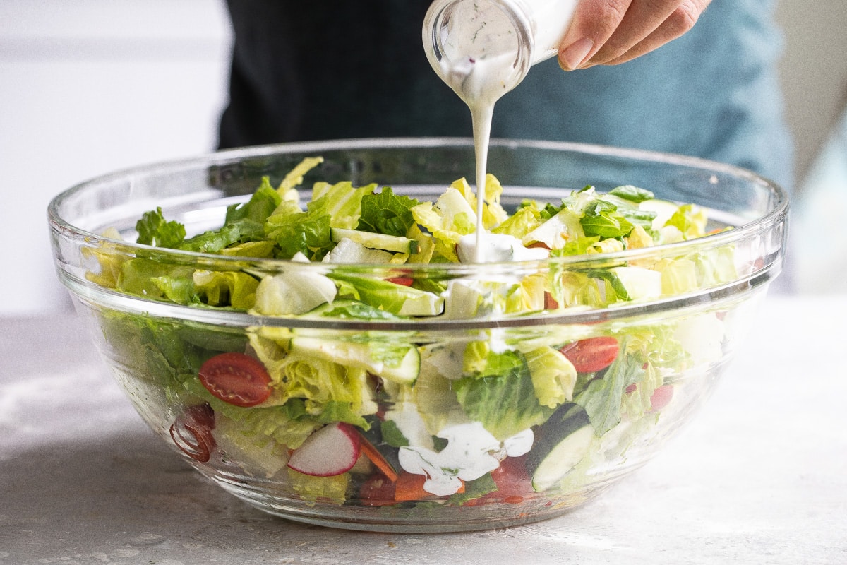 Drizzling ranch dressing over a garden salad.