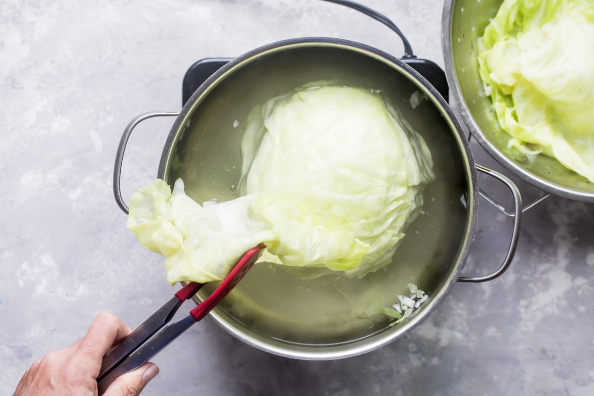A cabbage head being boiled and separated in a silver pot.