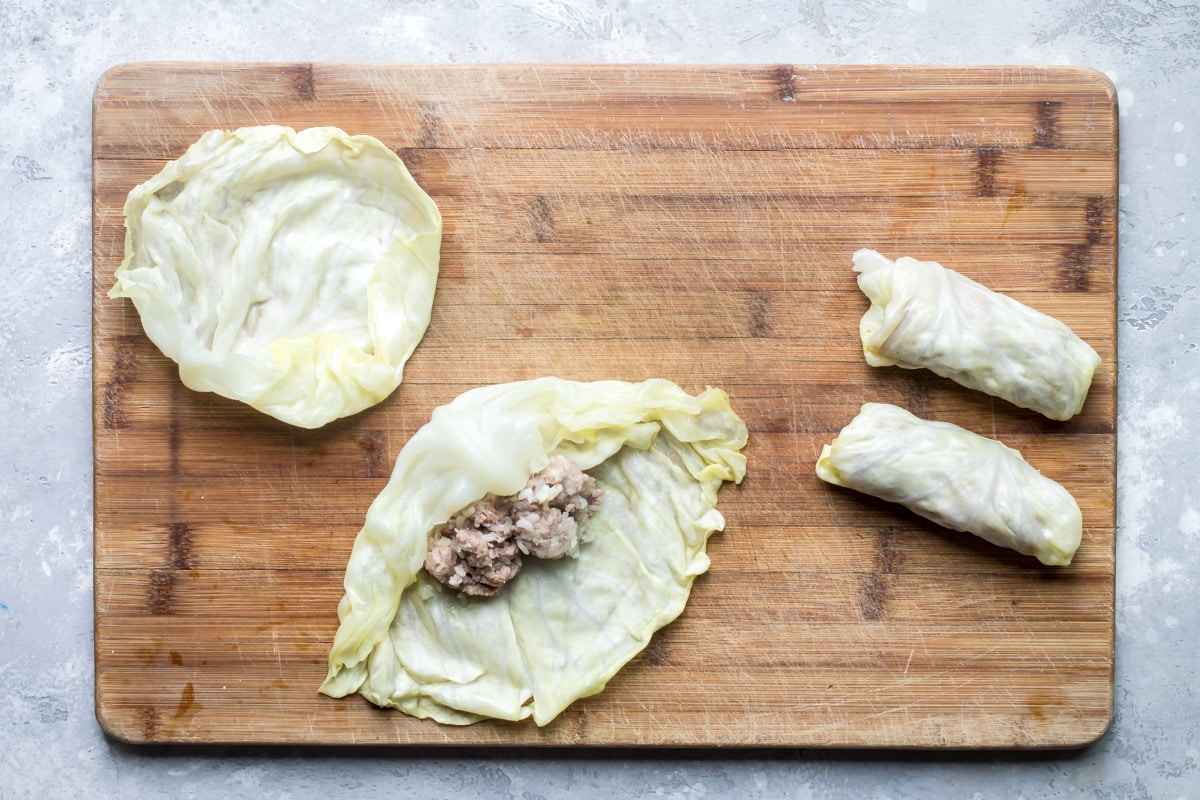 Cabbage rolls being stuffed and rolled on a wooden cutting board.