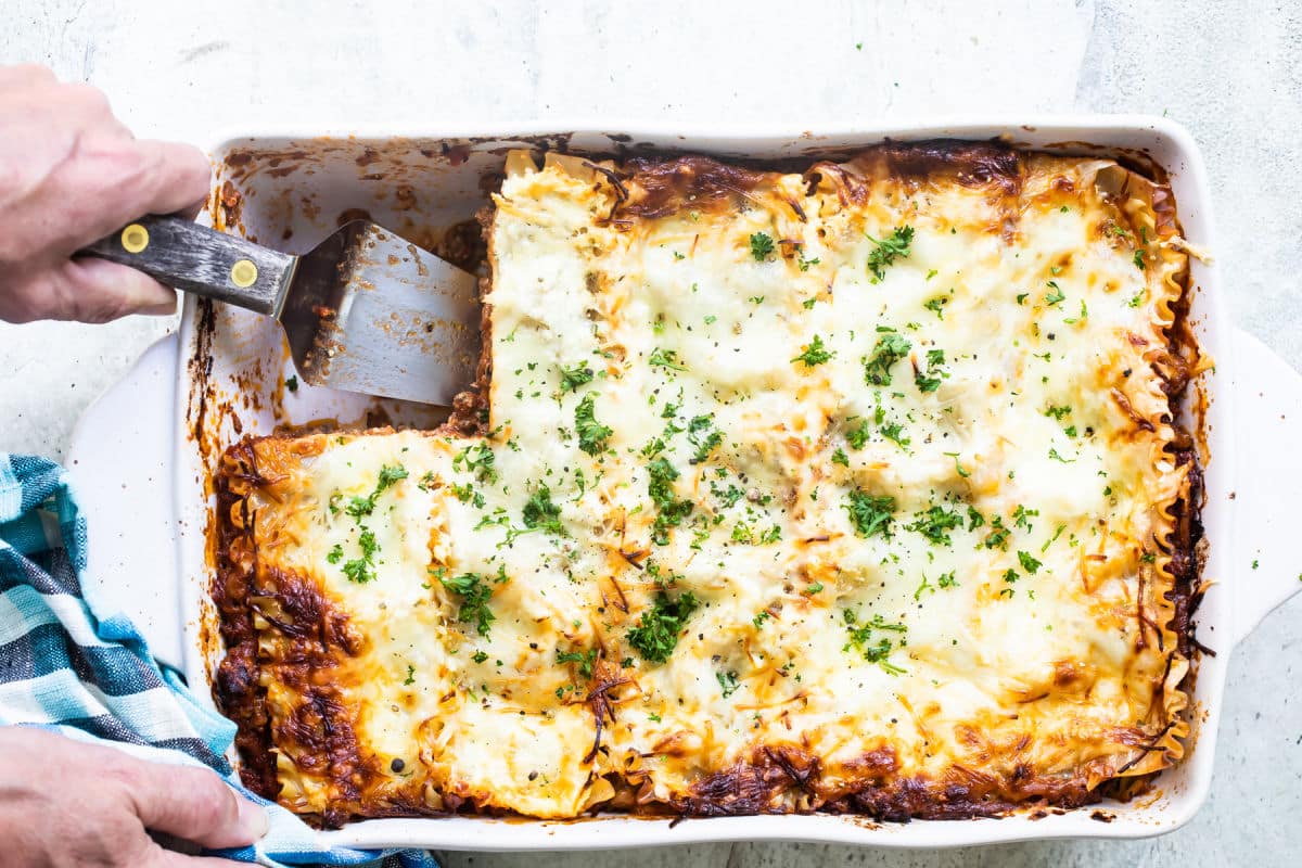 The best make ahead lasagna in a white baking dish with one piece removed.