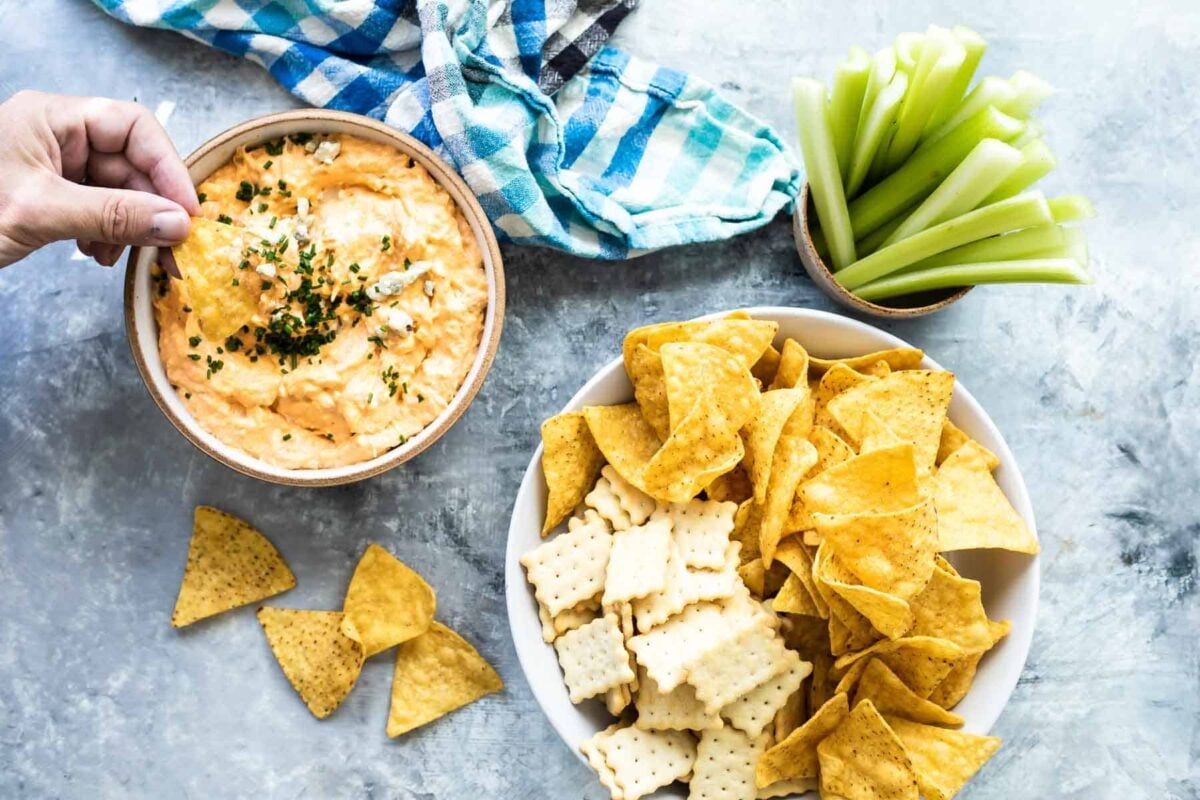 Buffalo chicken dip in a bowl with chips, crackers, and celery nearby.