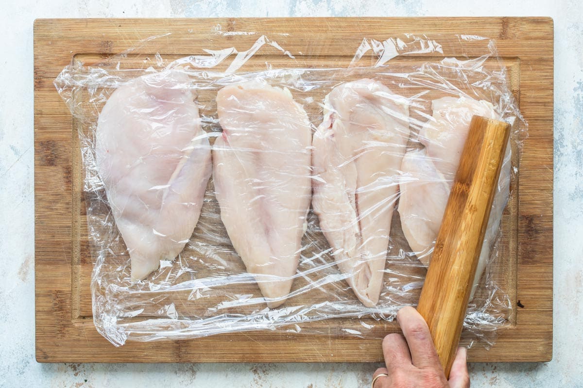 Pounding chicken cutlets thin under plastic wrap.
