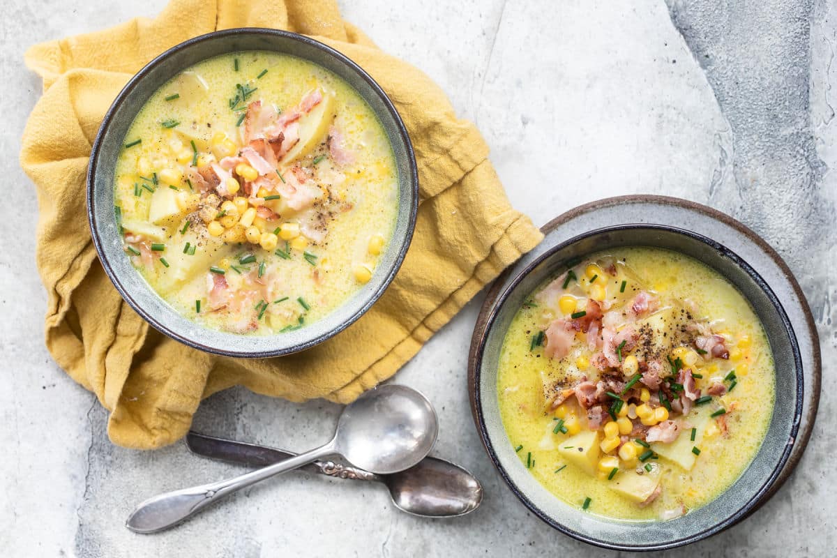 Two bowls of corn chowder on mustard-colored napkins.