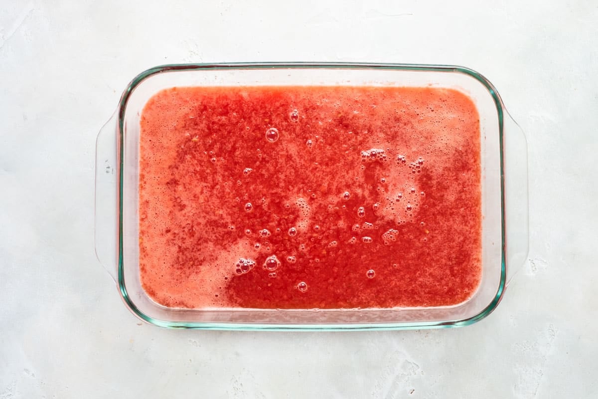 Pouring watermelon mixture into a glass dish to freeze for granita.