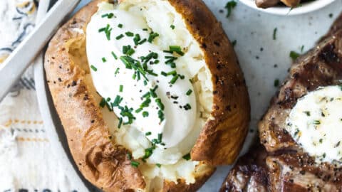 A plate with a baked potato topped with sour cream, a steak topped with butter, and a bowl of balsamic mushrooms on a plate.