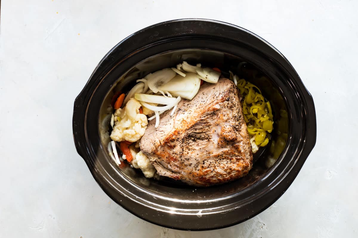 A browned beef roast in a slow cooker with pickled vegetables.