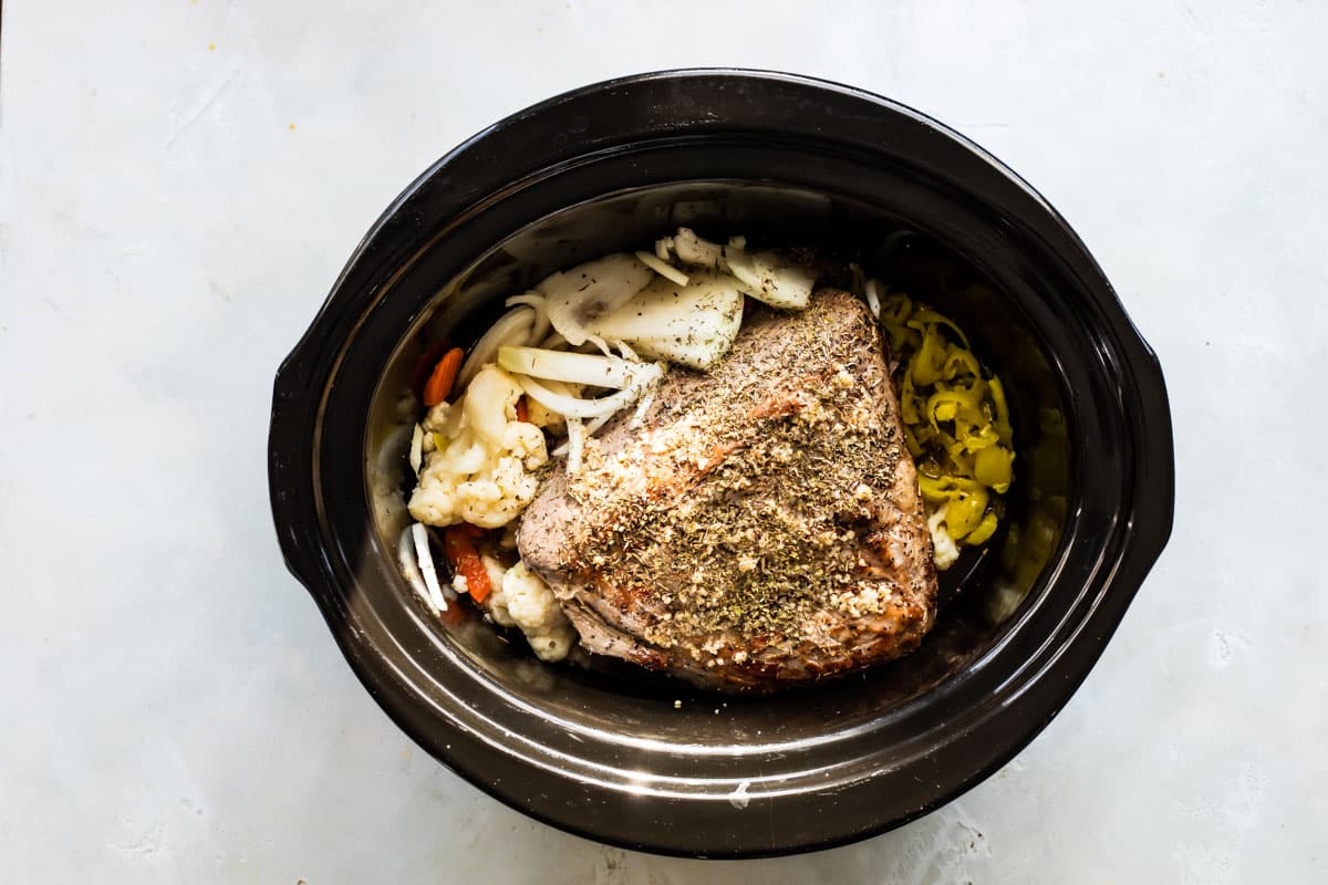 A browned beef roast in a slow cooker with pickled vegetables.