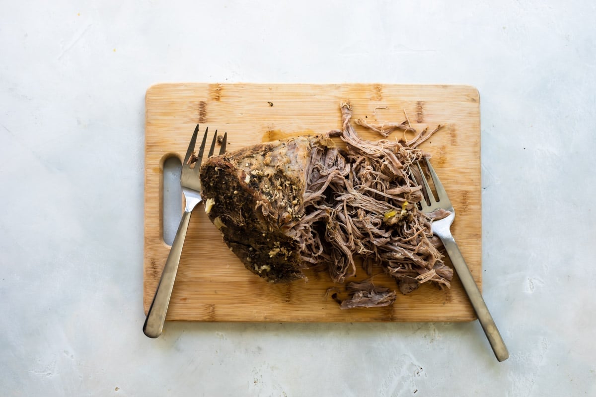 Shredded beef on a cutting board with 2 forks nearby.