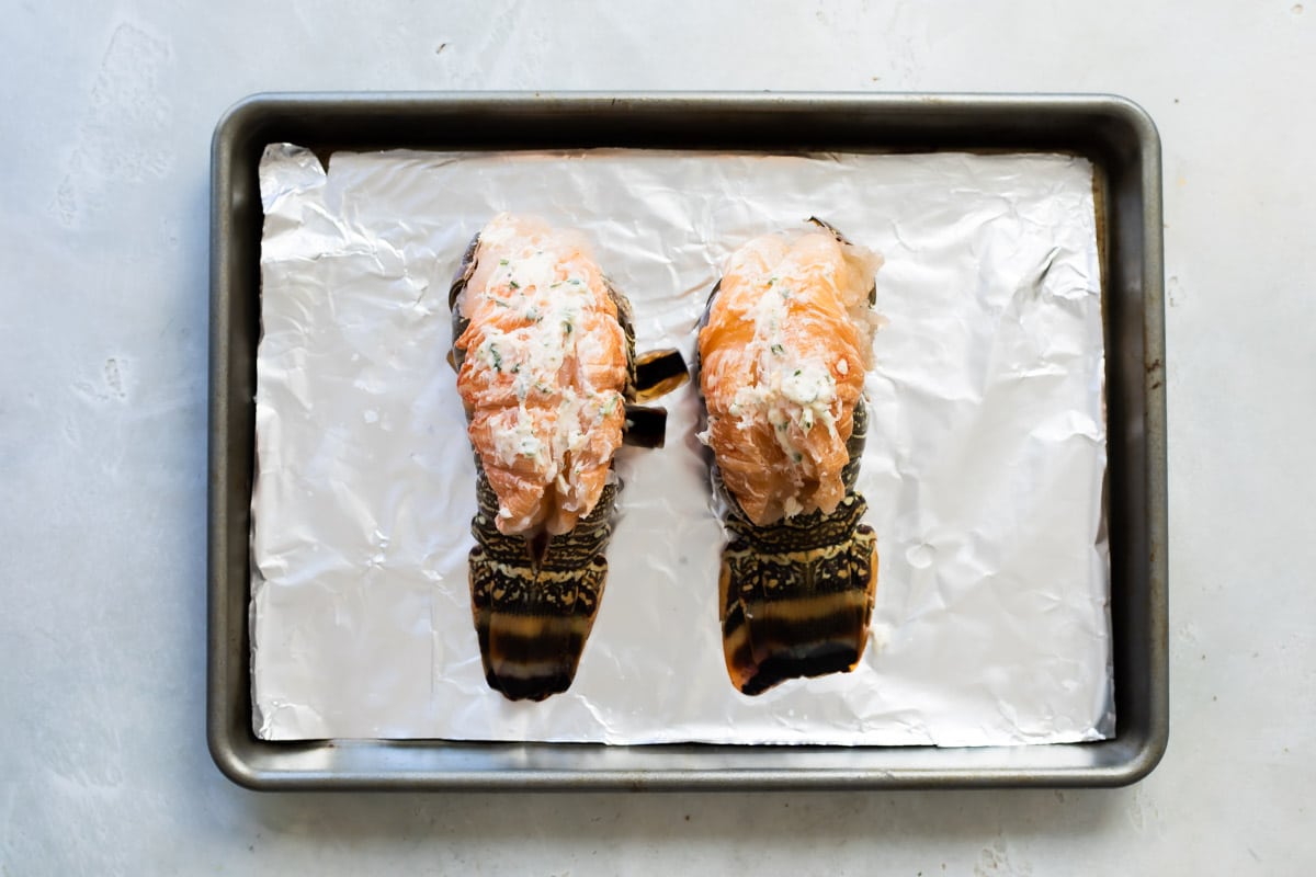 Raw lobster tails on a baking sheet.