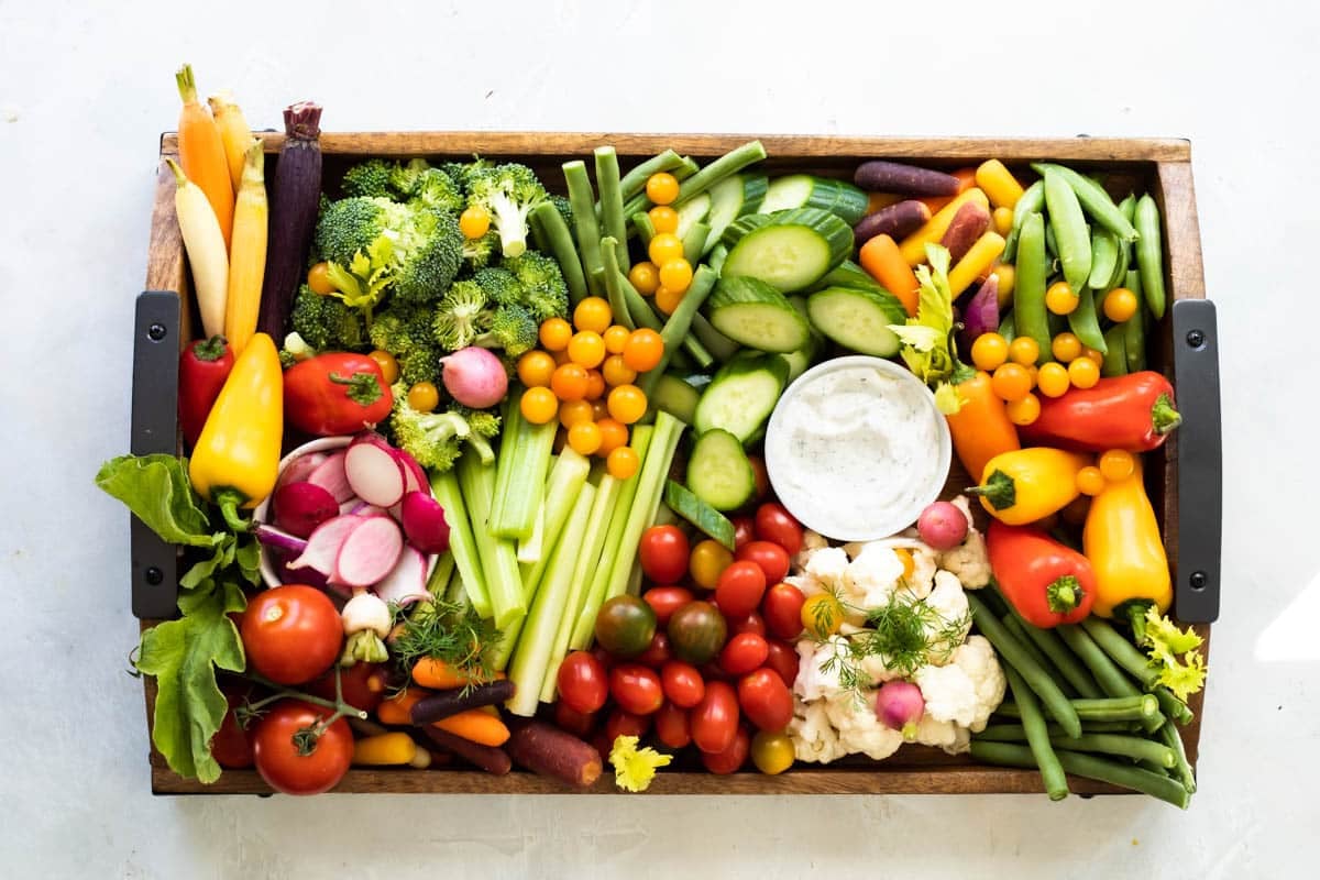 A platter full of fresh vegetables with a bowl of veggie dip.