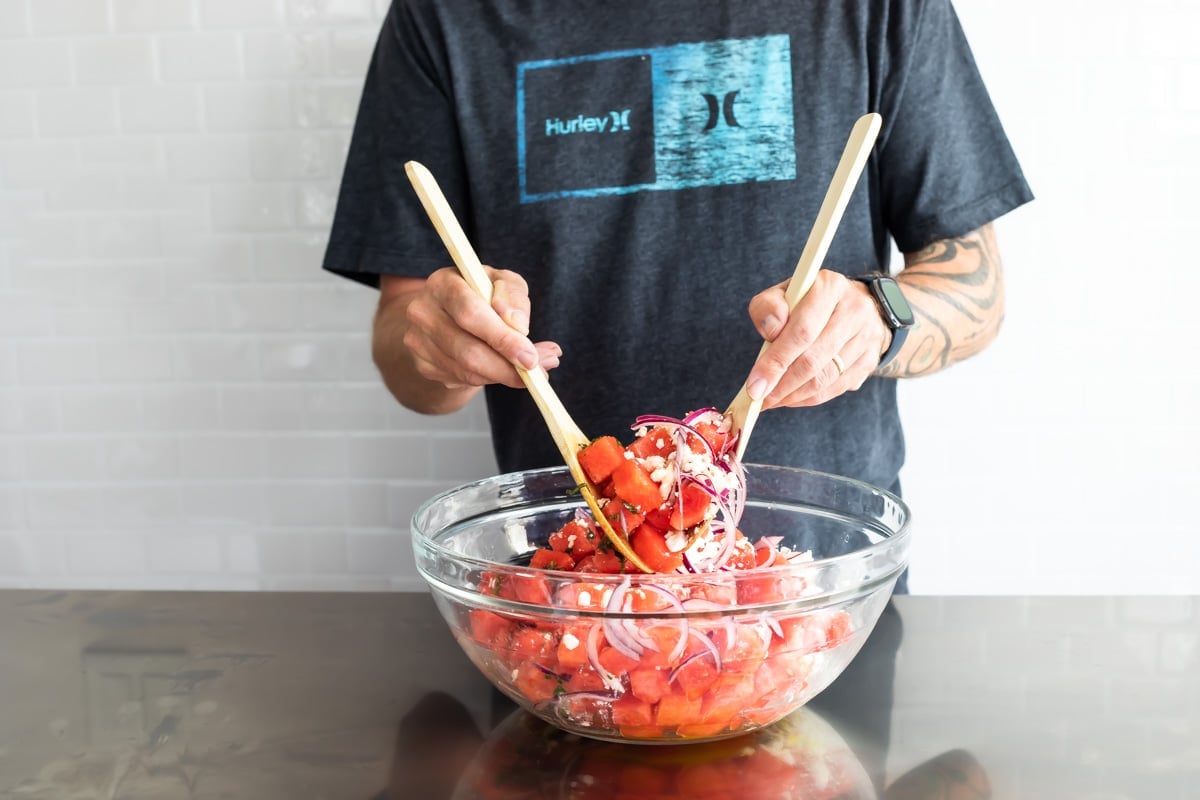 Tossing a watermelon salad in a glass bowl.