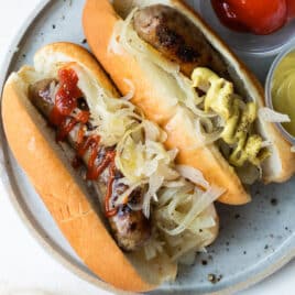 A plate of beer brats with ketchup, mustard, onions, and sauerkraut.