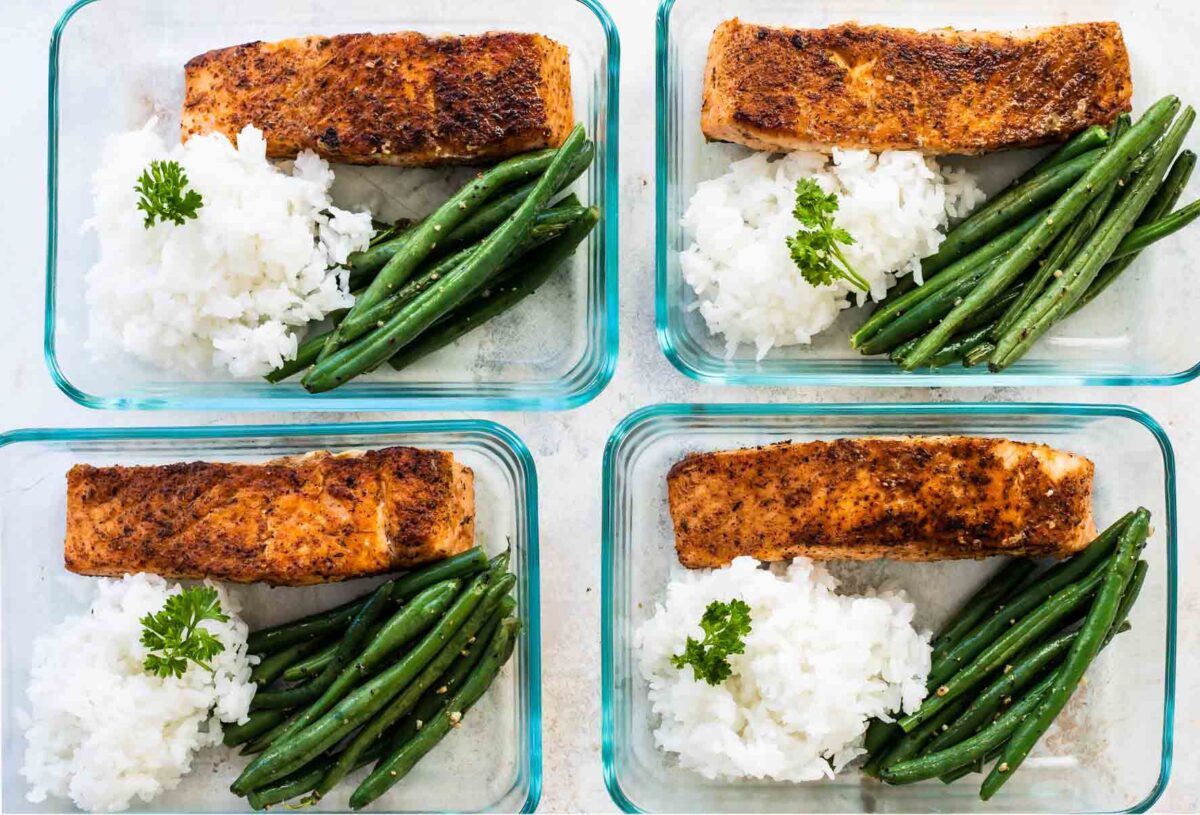 4 meal prep containers with blackened salmon, baked rice, and roasted green beans.