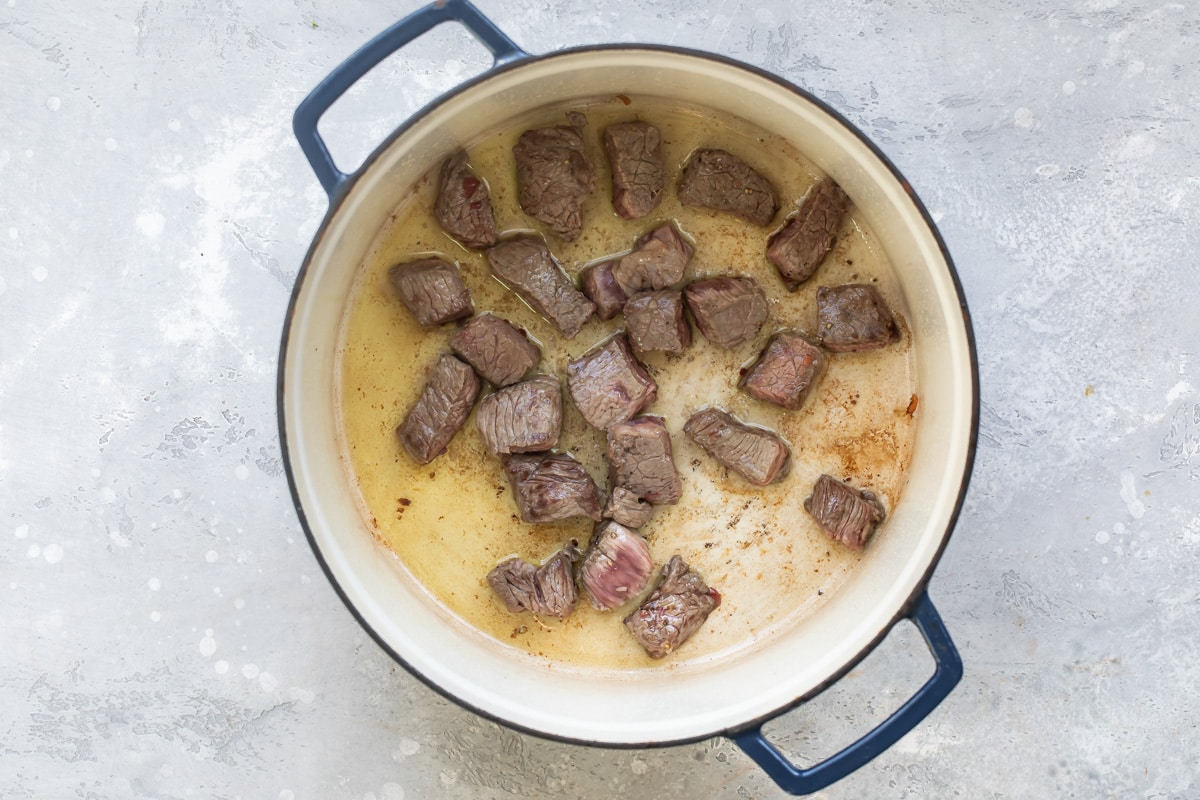 Pieces of beef cooking in a dutch oven.