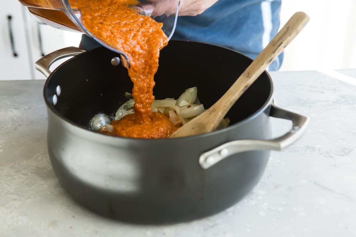 Tinga sauce being added to a saucepan with chicken.